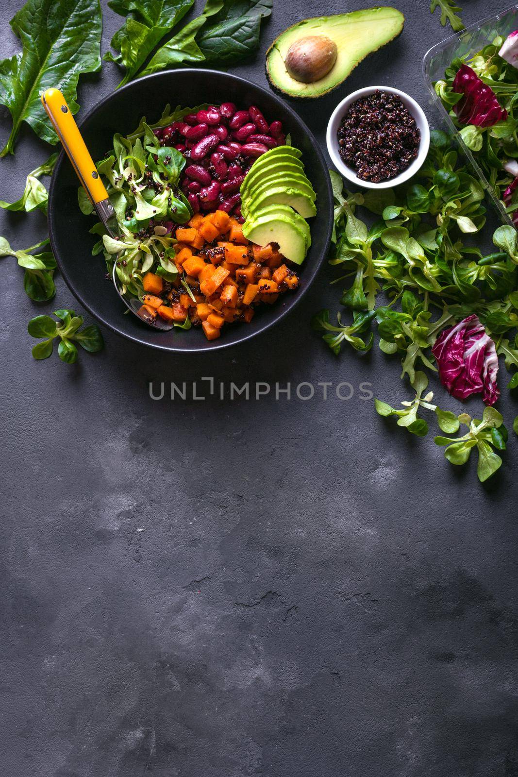 Quinoa salad in bowl with avocado, sweet potato, beans, herbs, spinat on concrete rustic background. Quinoa superfood concept. Clean healthy detox eating. Vegan/vegetarian food. Making healthy salad