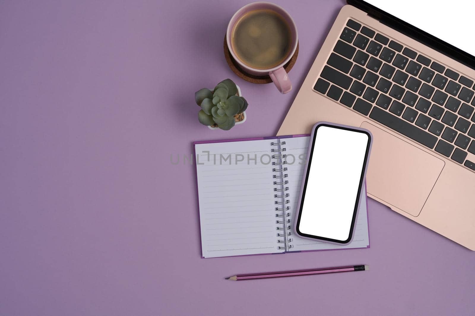Above view mobile phone, laptop, notebook and coffee cup on purple background.