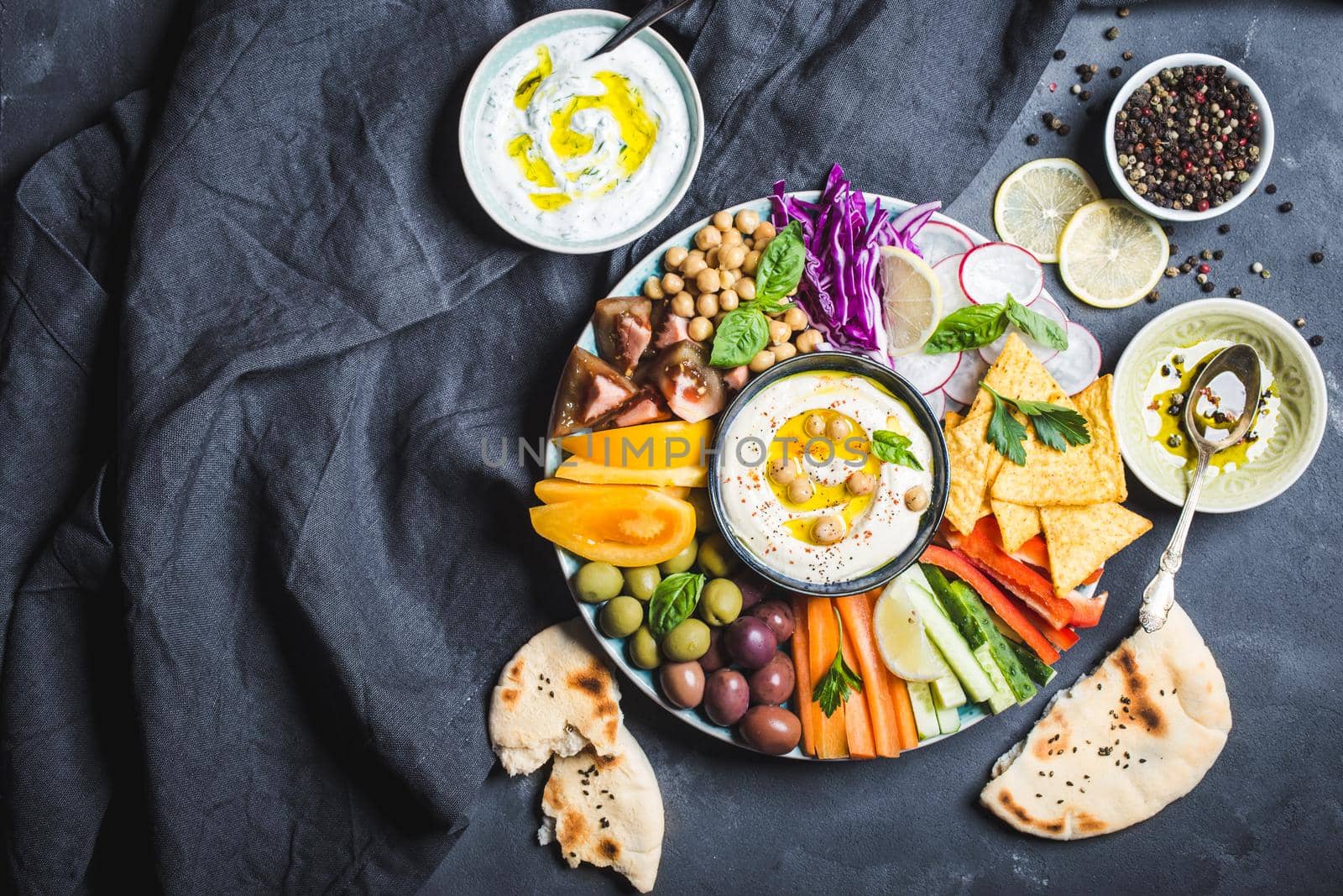 Meze platter with hummus, yoghurt dip, assorted snacks. Space for text. Hummus, vegetables sticks, chickpeas, olives, pita, chips. Plate, Middle Eastern/Mediterranean meze. Party/finger food. Top view