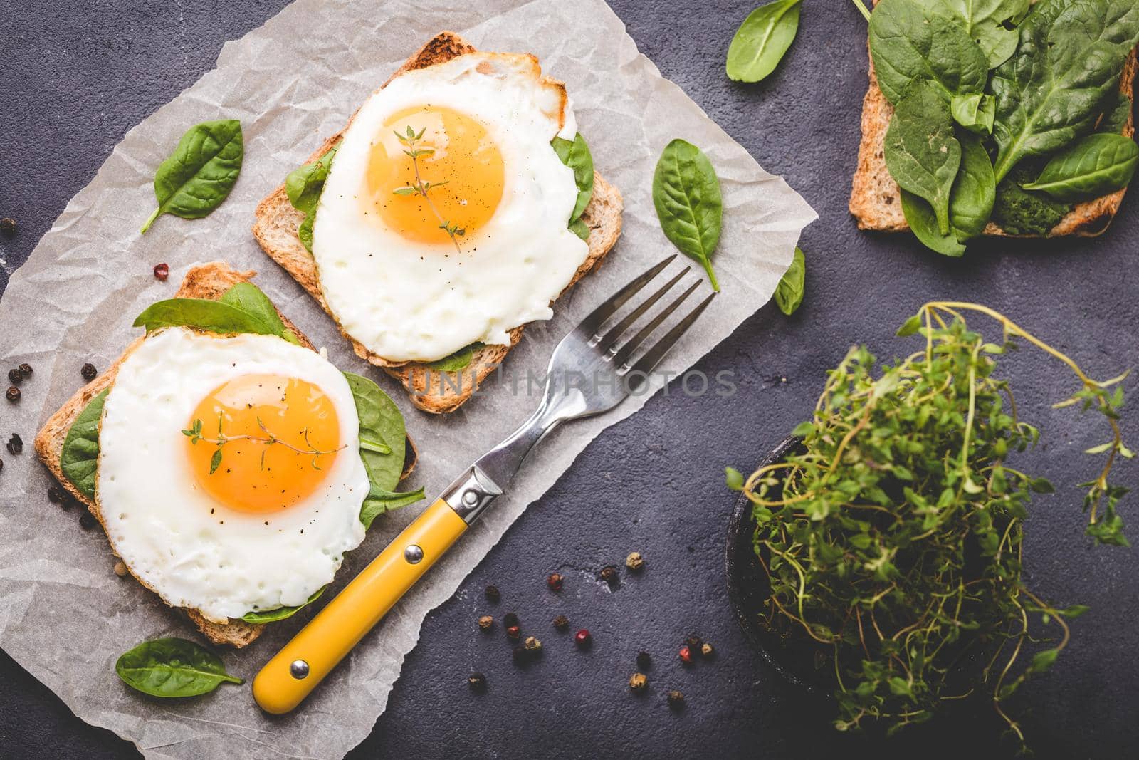 Healthy sandwich with wholegrain toast, fried egg, fresh spinach, thyme on rustic stone background. Egg sandwich for morning breakfast. Clean healthy eating concept. Vegetarian lunch/snack. Top view