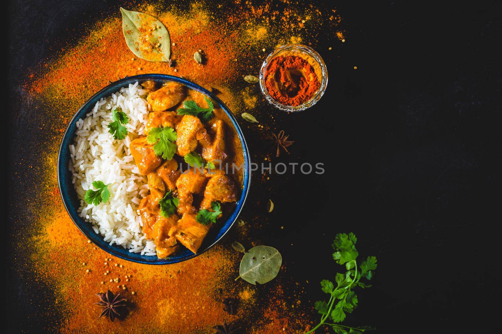 Indian Butter chicken with basmati rice in bowl, spices, black background. Space for text. Butter chicken, traditional Indian dish. Top view. Chicken tikka masala. Indian cuisine concept. Overhead