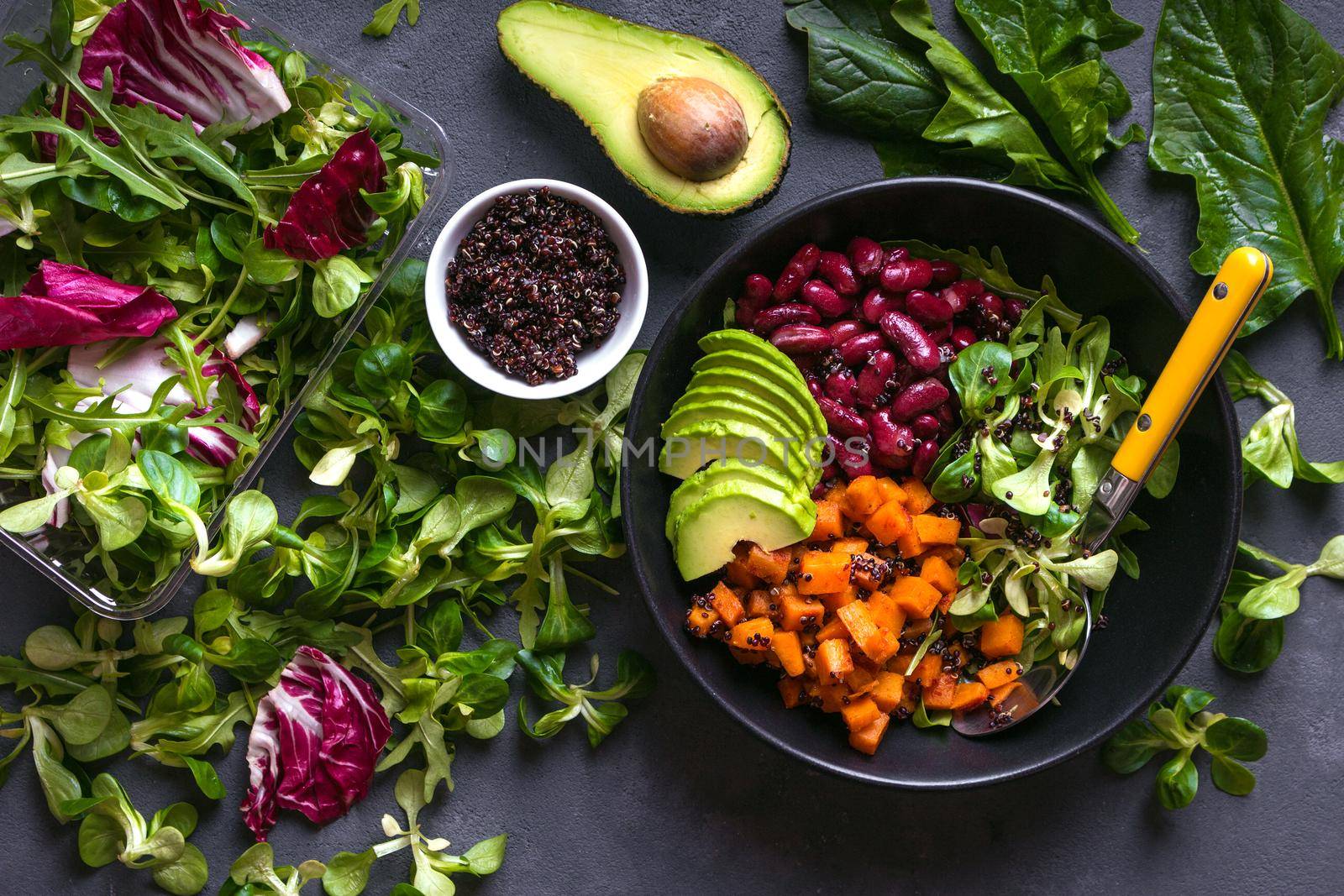 Quinoa salad in bowl with avocado, sweet potato, beans, herbs, spinat on concrete rustic background. Quinoa superfood concept. Clean healthy detox eating. Vegan/vegetarian food. Making healthy salad