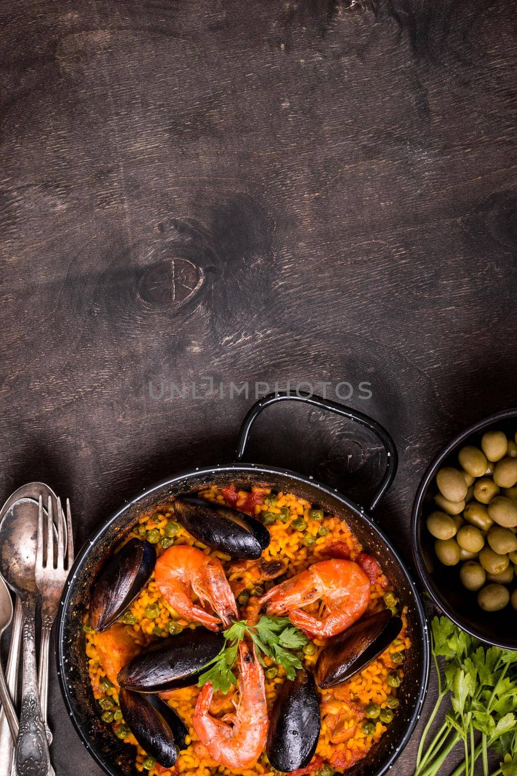 Paella background, space for text. Paella in black pan with saffron rice, peas, shrimps, mussels, squid, meat. Seafood paella, traditional spanish dish. Paella on rustic black wooden table. Top view