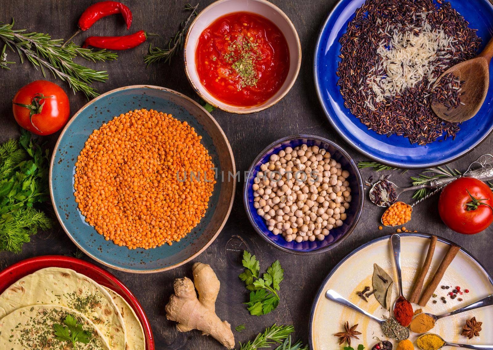 Table served with traditional for asian or eastern cuisine food. Cereal grains, beans, spices on colorful plates. Lentil, basmati and wild rice mix, chick-pea, tomato chutney, pita. Ingredients for indian or eastern food
