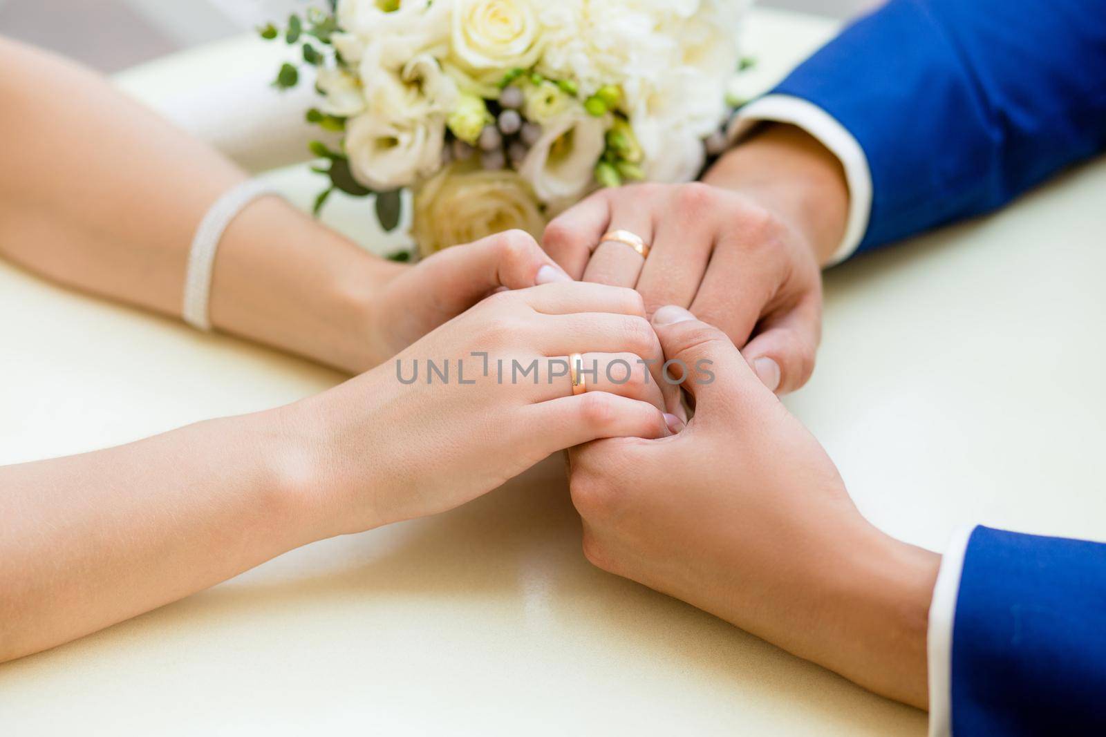 Close-up of wedding hands with rings and bouquet lie on the table