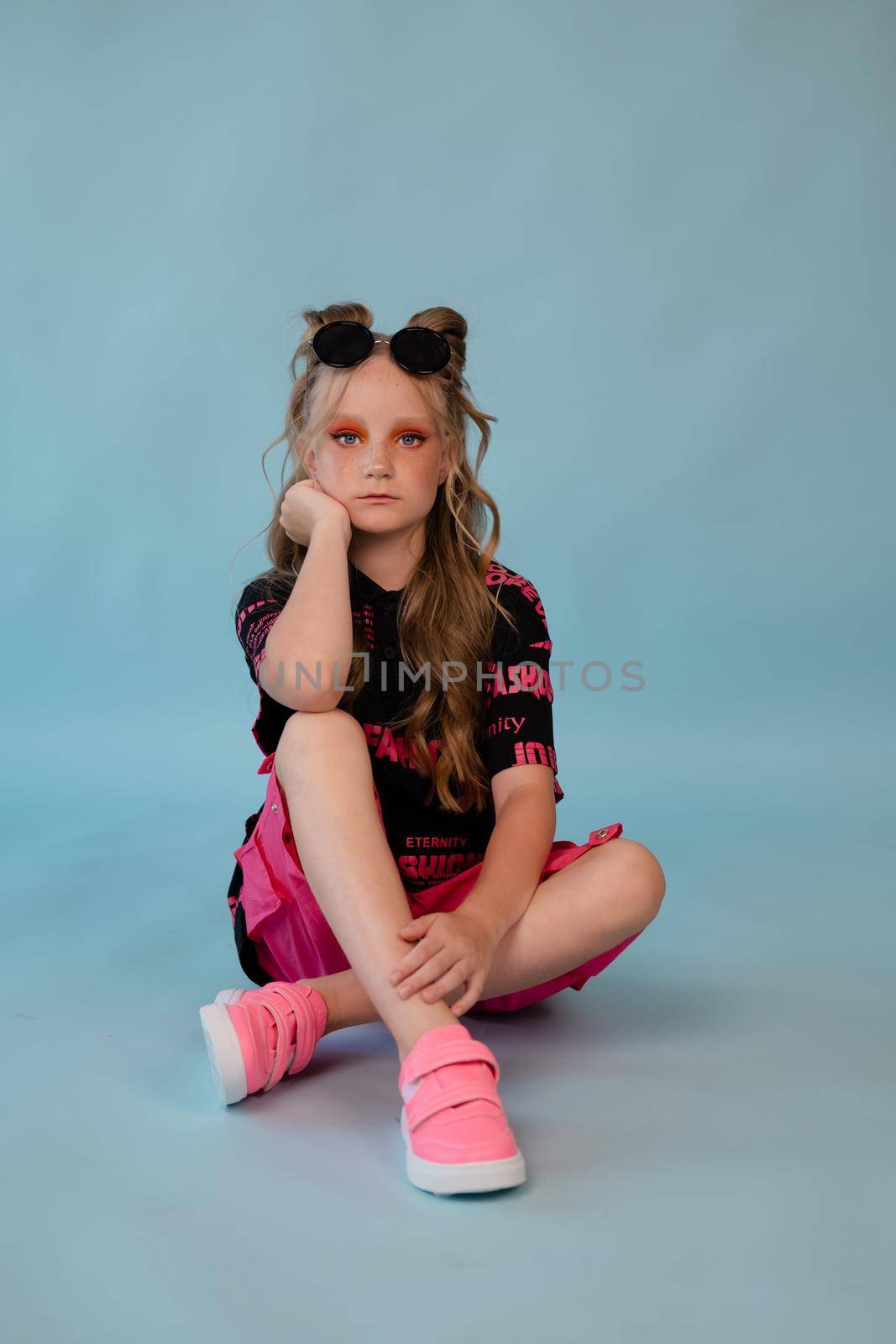 stylish teenage girl. tween school girl wearing pink fashion clothes on blue background. long hair and freckles.