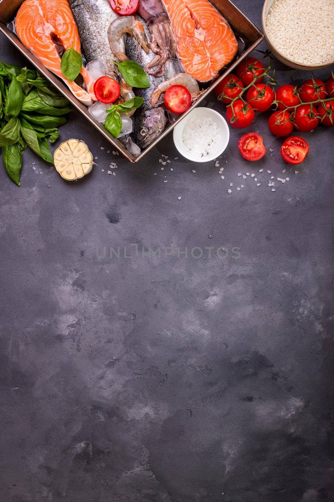 Assorted fish and seafood. Raw fresh salmon steak, trout, squid, shrimps with vegetables and rice ready to cook. Ingredients for cooking on concrete background. Space for text. Diet and healthy food