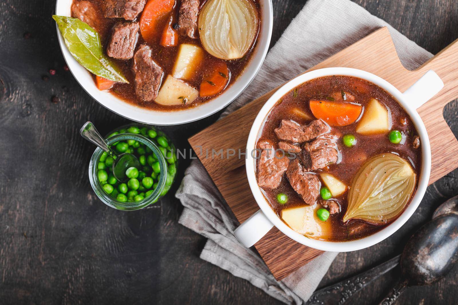 Meat stew with beef, potato, carrot, onion, spices. green peas. Slow cooked meat stew in bowl, wooden background. Hot autumn/winter dish. Closeup. Top view. Space for text. Comfort food. Homemade soup