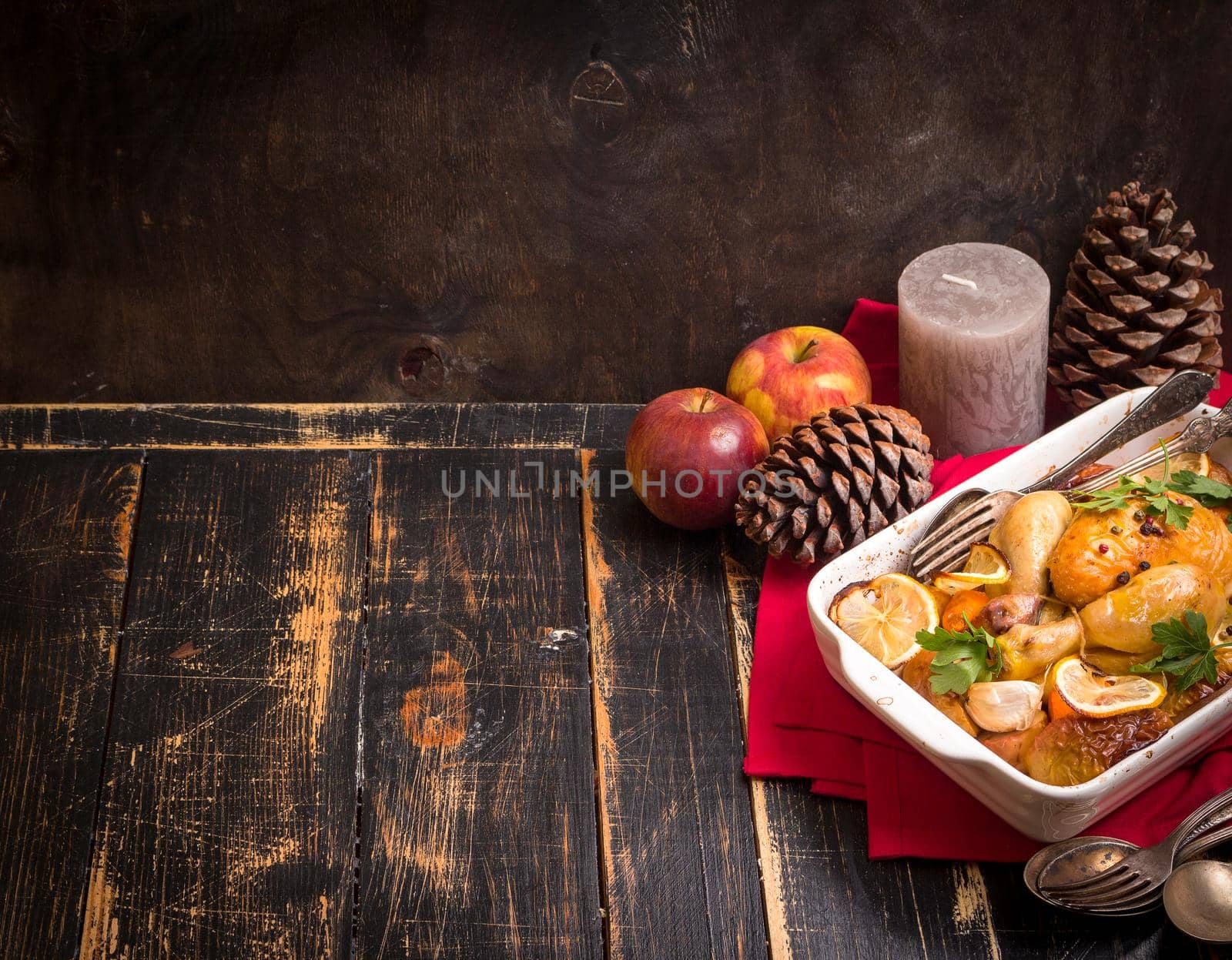 Roasted chicken. Christmas food background. Rustic celebration table with roasted chicken, vegetables, apples, decorated with candles, vintage cutlery. Christmas/Thanksgiving dinner. Space for text