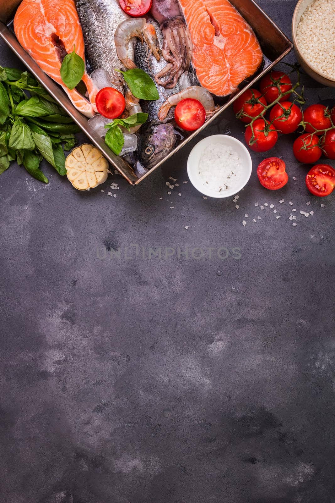 Assorted fish and seafood. Raw fresh salmon steak, trout, squid, shrimps with vegetables and rice ready to cook. Ingredients for cooking on concrete background. Space for text. Diet and healthy food
