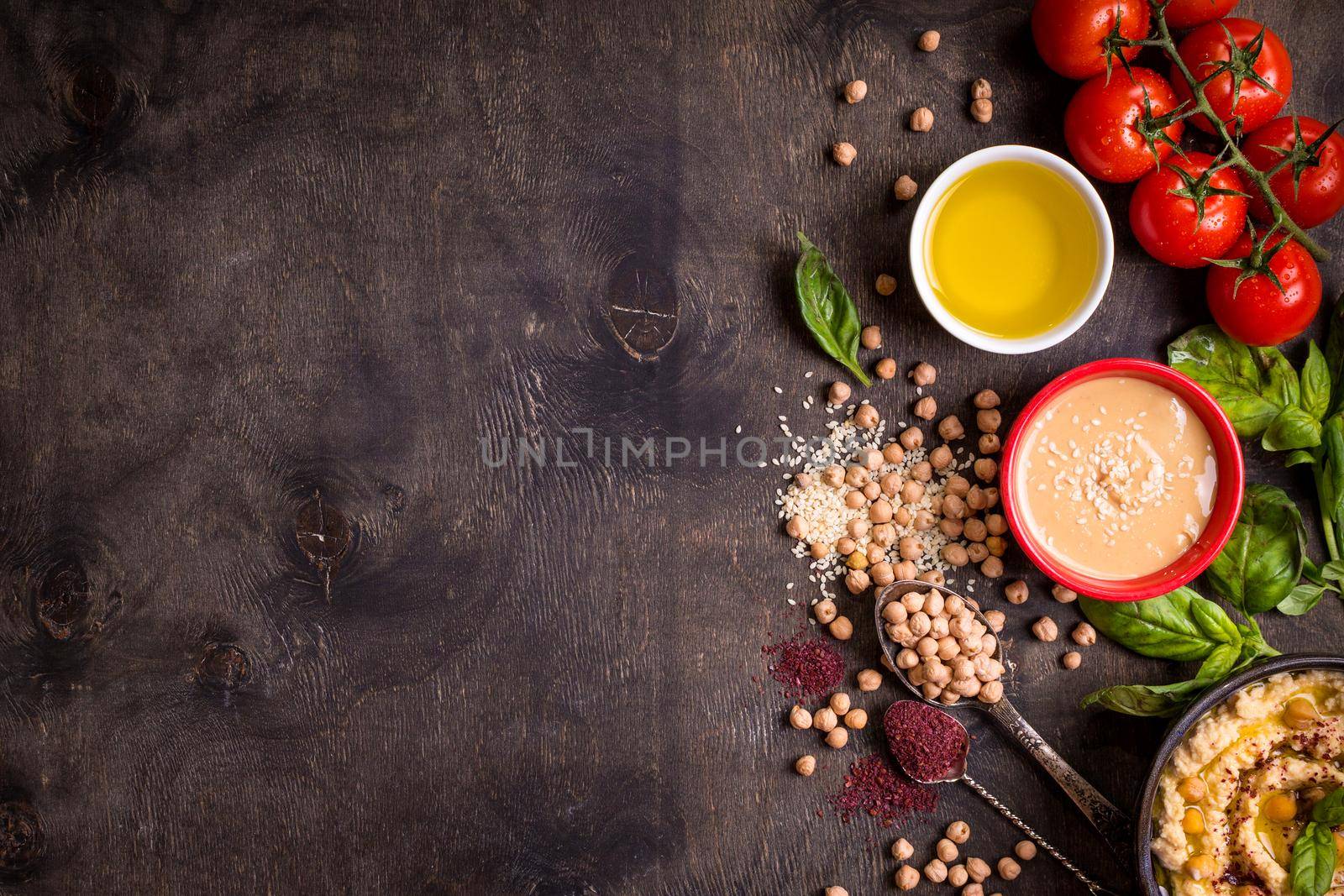 Hummus ingredients. Chickpea, tahini, olive oil, sesame seeds, sumac, herbs on dark rustic wooden background. Space for text. Set of ingredients for making hummus. Middle eastern cuisine. Top view