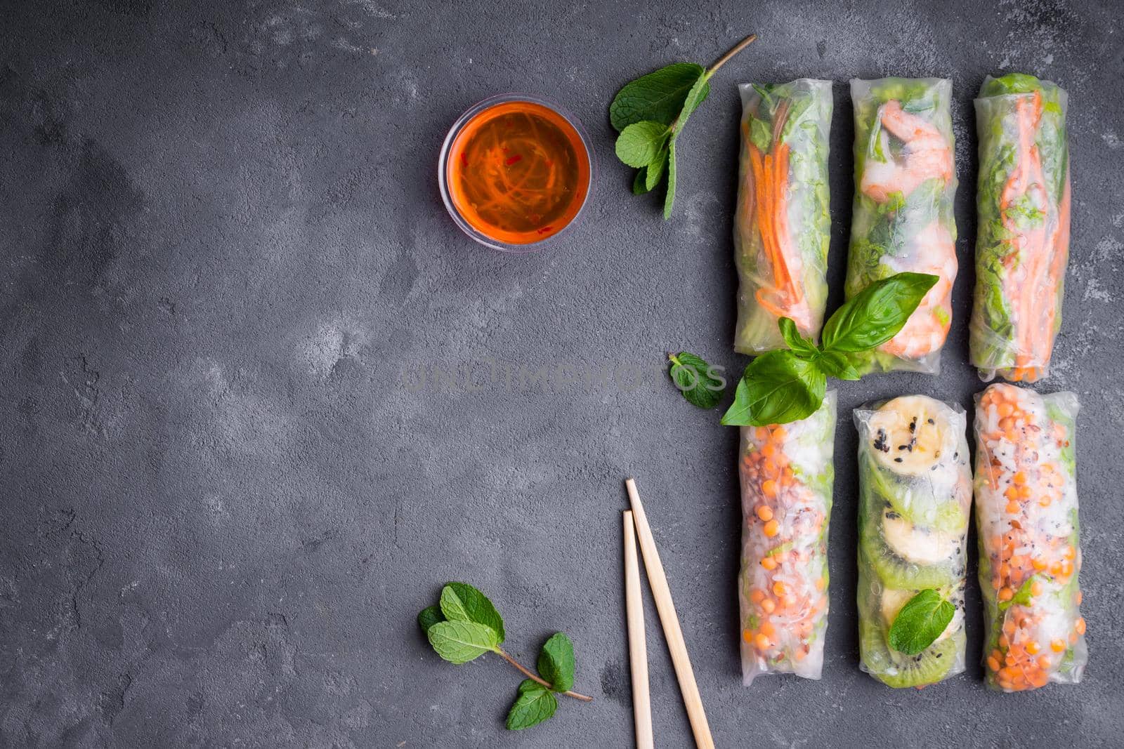 Fresh assorted spring rolls set background. Handmade asian/Chinese spring rolls, sauce, chopsticks. Rustic concrete background. Spring rolls with shrimps, vegetables, fruits. Space for text. Top view
