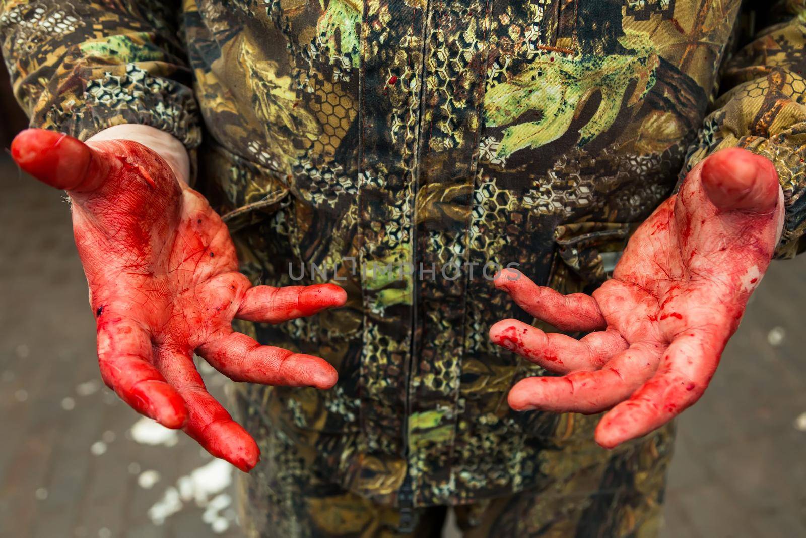 Male hands covered in blood. The hands of a soldier or a hunter are stained with blood. A man in camouflage clothes shows the bloody palms of his hands