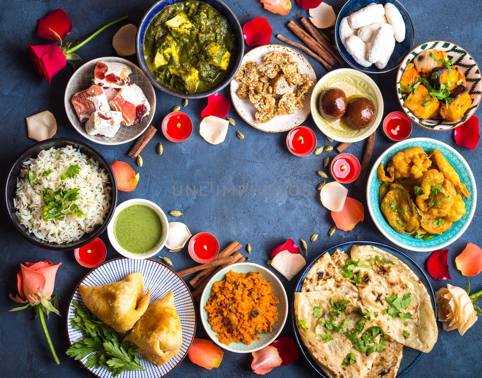 Festive food for Indian festival Diwali. Naan, samosa, rice, paneer, sweets. Background. Holiday Indian table with food, sweets, flowers, burning candles. Diwali celebratory dinner. Space for text.