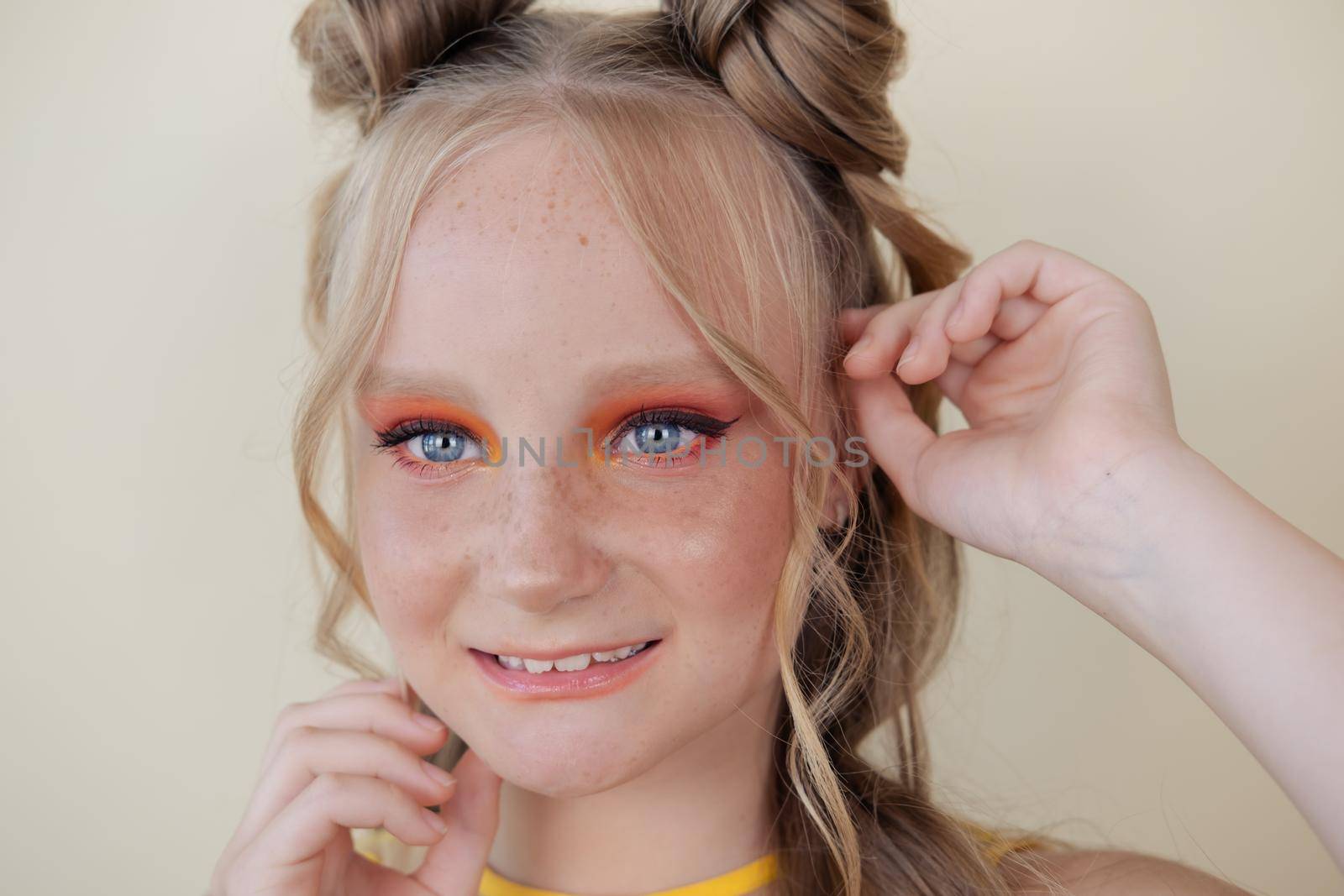charming blonde tween girl with orange makeup on yellow background. teenager portrait.