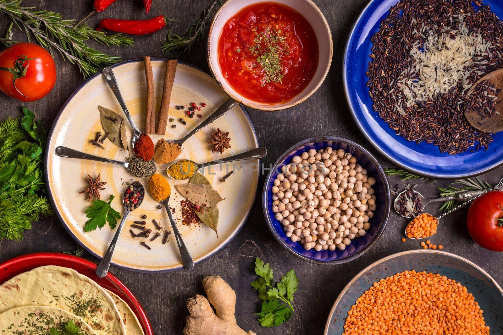 Assorted spices, herbs, chick-pea, lentil, basmati and wild rice mix, tomato chutney and pita on colorful plates. Top view. Spices and different food. Indian/ayurvedic food...