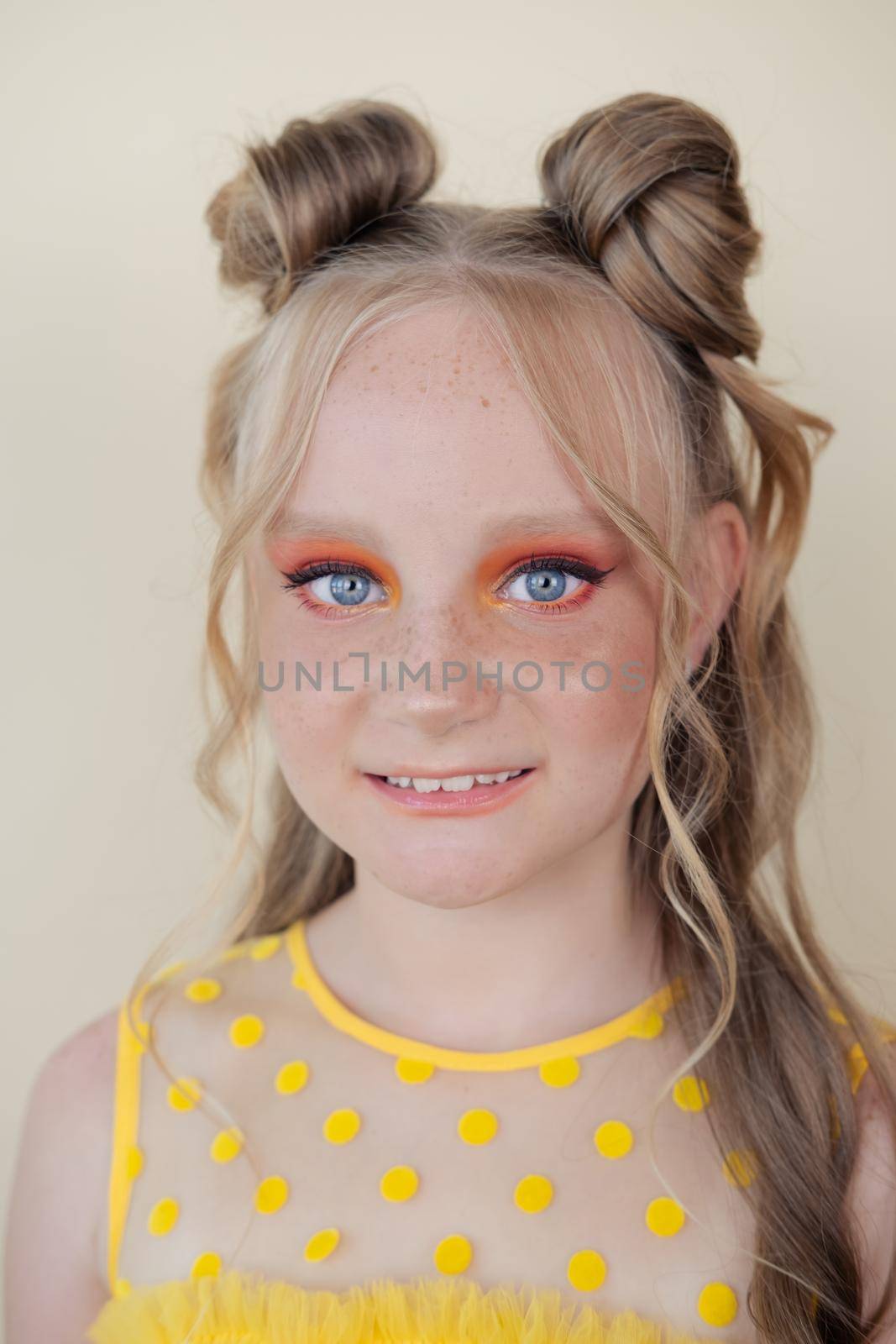 charming blonde tween girl with orange makeup on yellow background. teenager portrait by oliavesna