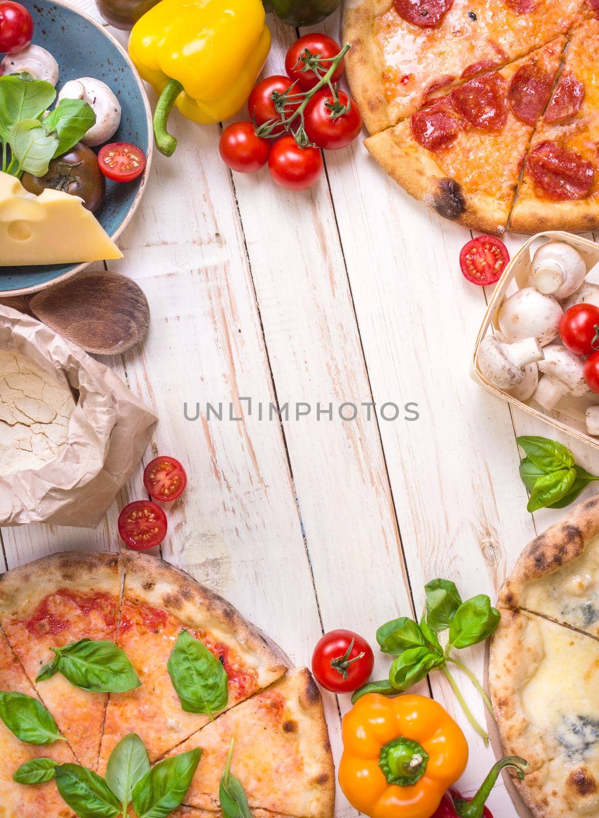 Pizza with assorted toppings and ingredients background. Space for text. Pizza, flour, cheese, tomatoes, basil, pepperoni, mushrooms and rolling pin over white wooden background. Top view. Food frame