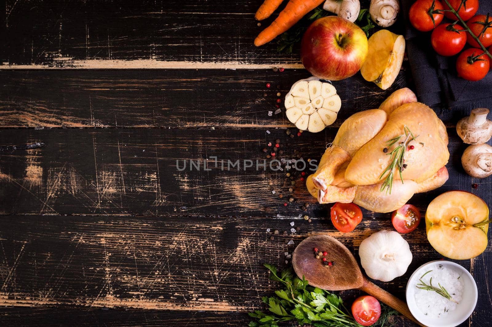 Raw whole chicken ready for cooking. Chicken with vegetables, herbs and spices on a black rustic wooden background. Space for text. Food frame. Diet or healthy eating. Ingredientd for cooking