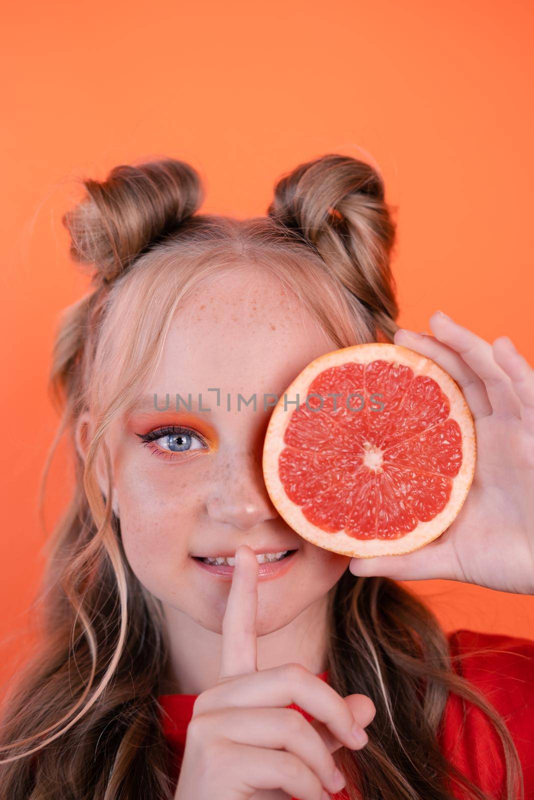 pretty tween girl in orange with a grapefruit isolated on orange background. tropical citrus fruit Grapefruit slices. orange stylish make up. teenager portrait by oliavesna