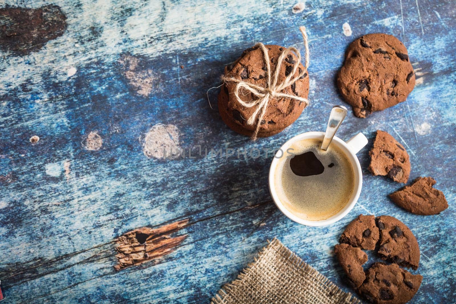 Cup of fresh hot coffee, chocolate cookies on old rustic blue wooden table. Vintage background. Space for text. Morning coffee. Warm coffee, dessert for lunch. Espresso, white cup. Top view. Close up