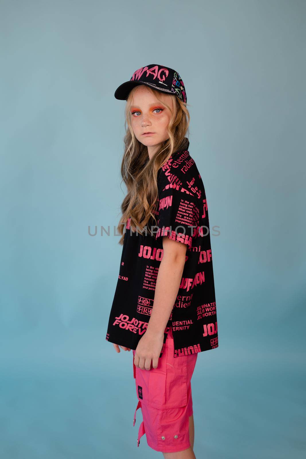 stylish teenage girl. tween school girl wearing pink fashion clothes on blue background. long hair and freckles.