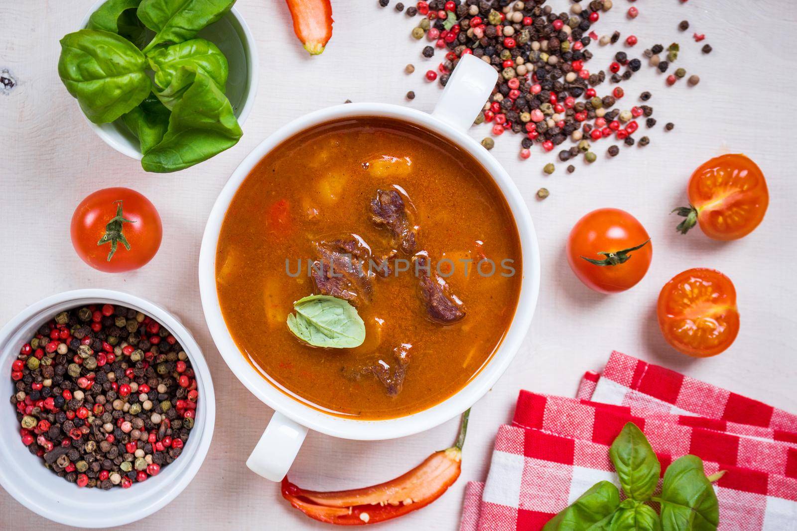 Delicious tomato soup with meat on a white rustic wooden table with fresh cherry tomatoes, basil leaves and dry pepper. Ingredients for soup. Top view