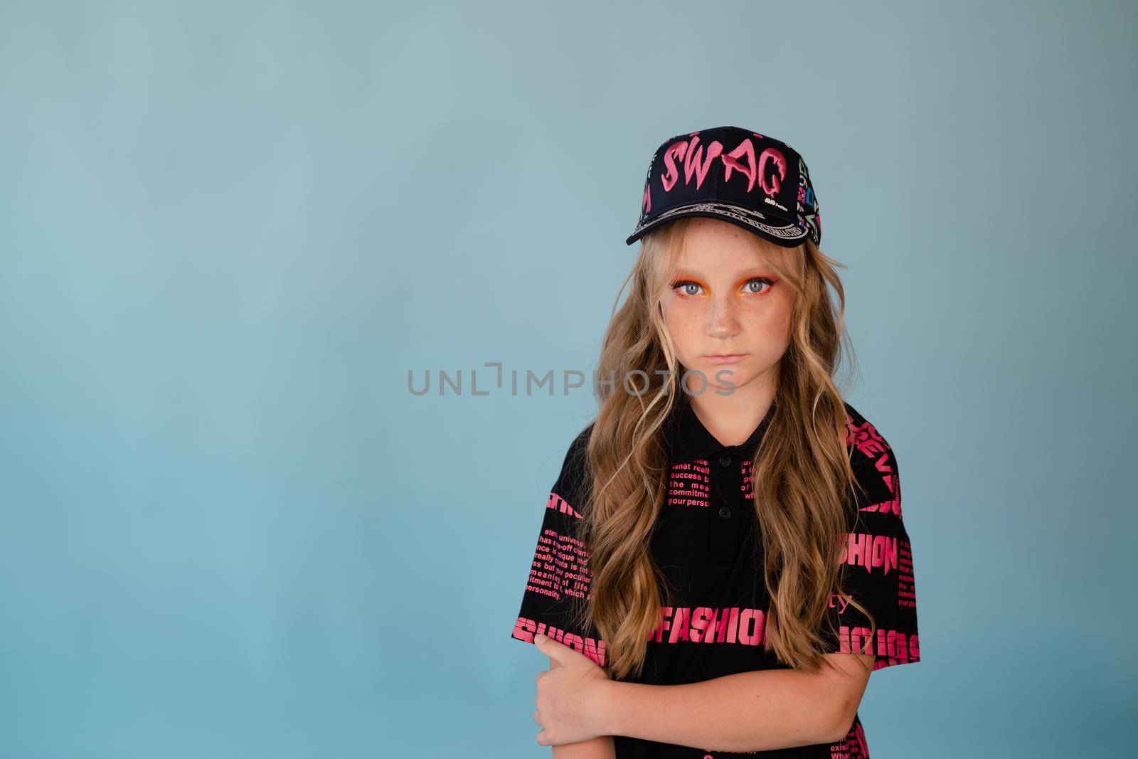 fashion teenager portrait. tween school girl with orange makeup wearing pink stylish cool clothes on blue background.