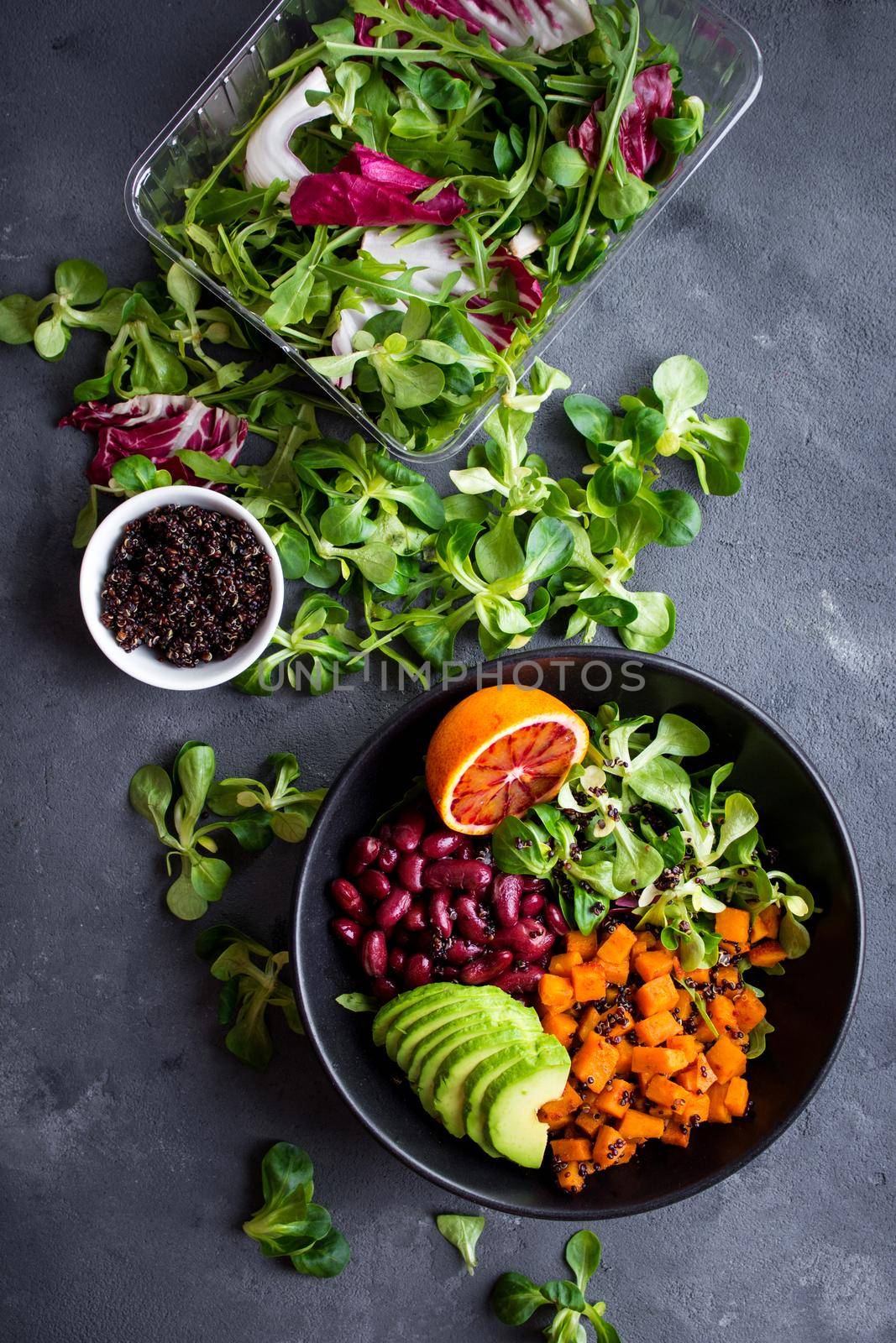 Quinoa salad in bowl with avocado, sweet potato, beans, herbs, orange on concrete rustic background. Quinoa superfood concept. Clean healthy detox eating. Vegan/vegetarian food. Making healthy salad