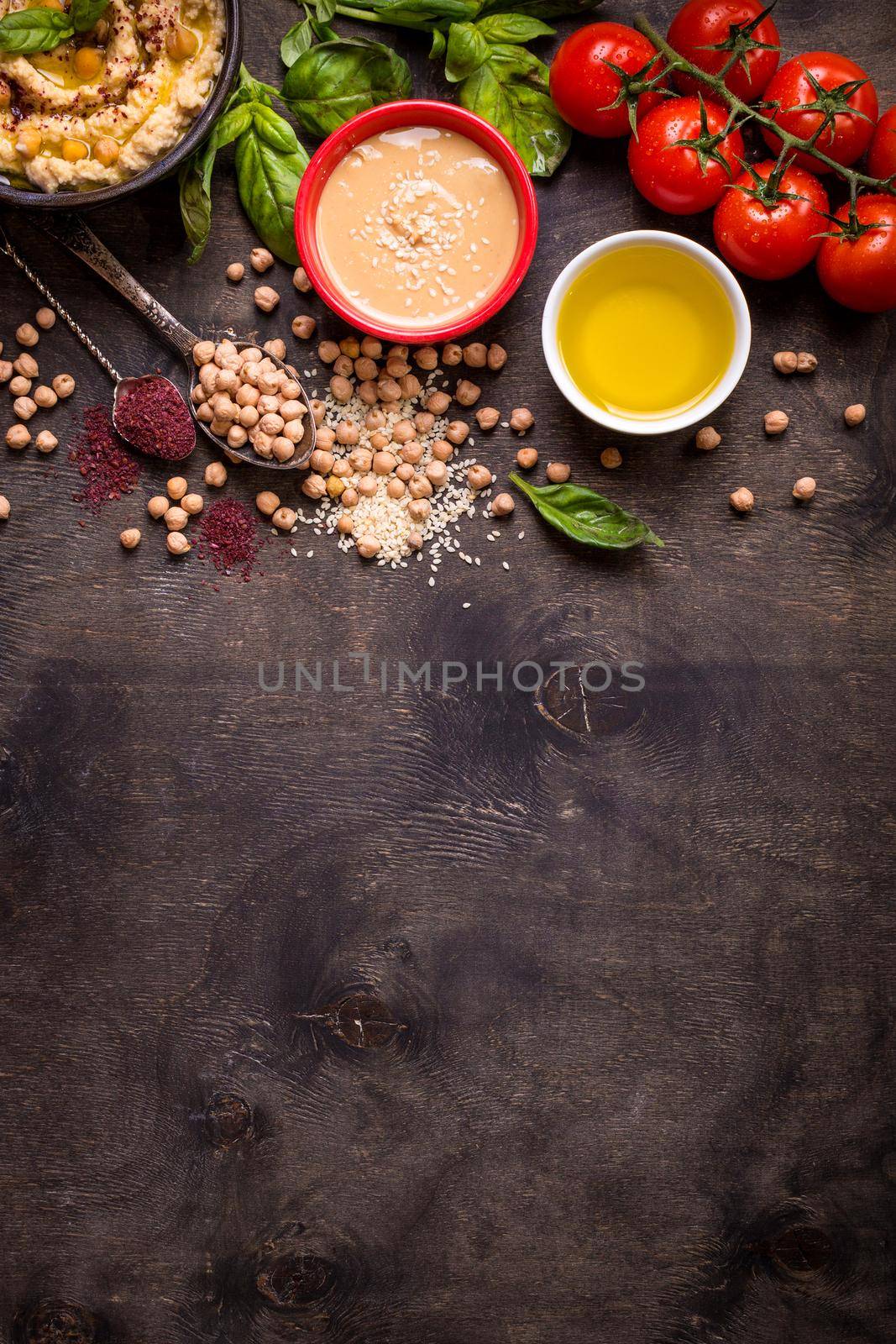 Hummus ingredients. Chickpea, tahini, olive oil, sesame seeds, sumac, herbs on dark rustic wooden background. Space for text. Set of ingredients for making hummus. Middle eastern cuisine. Top view