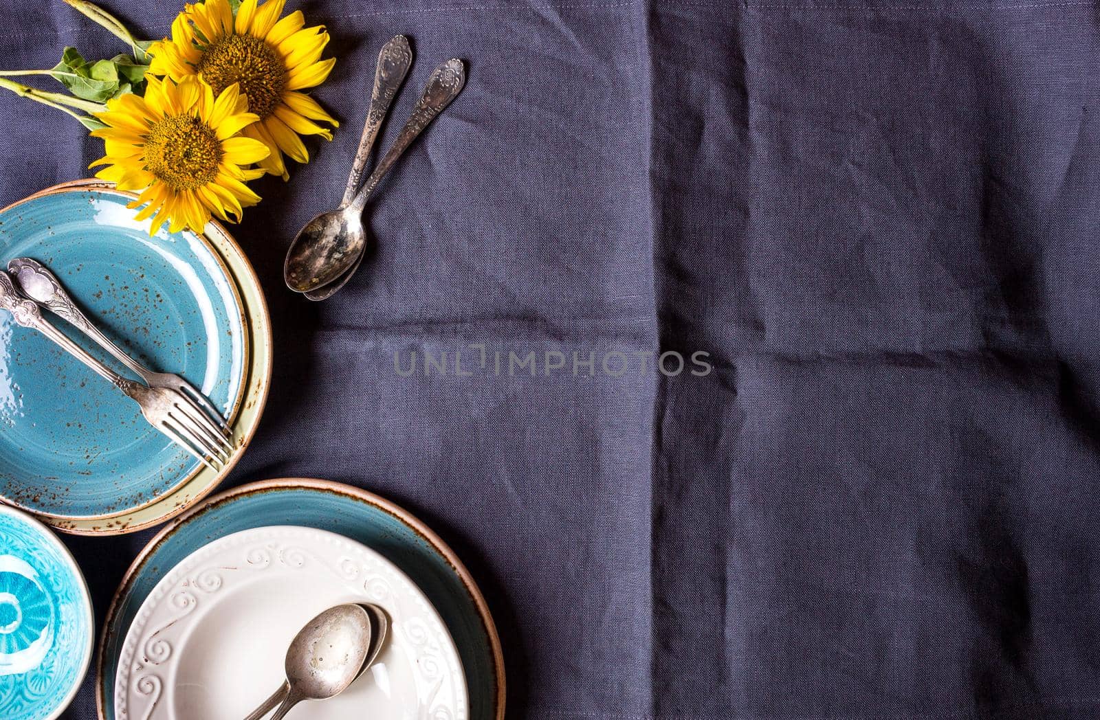 Vintage multicolored empty plates and bowls on a dark gray linen tablecloth with sunflower. With antique spoons and forks. Space for text. Table setting. Shabby chic/retro style. Top view. Copy space