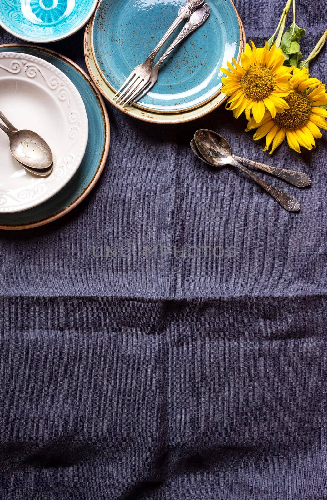 Vintage multicolored empty plates and bowls on a dark gray linen tablecloth with sunflower. With antique spoons and forks. Space for text. Table setting. Shabby chic/retro style. Top view. Copy space