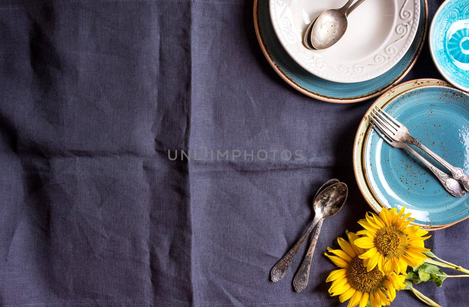 Vintage multicolored empty plates and bowls on a dark gray linen tablecloth with sunflower. With antique spoons and forks. Space for text. Table setting. Shabby chic/retro style. Top view. Copy space