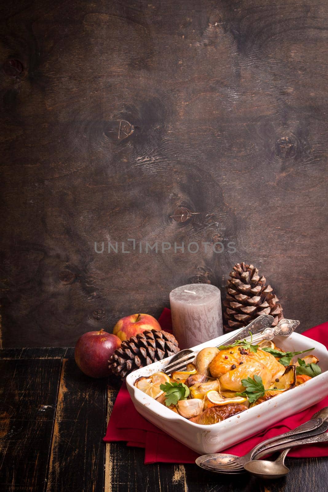 Roasted chicken. Christmas food background. Rustic celebration table with roasted chicken, vegetables, apples, decorated with candles, vintage cutlery. Christmas/Thanksgiving dinner. Space for text