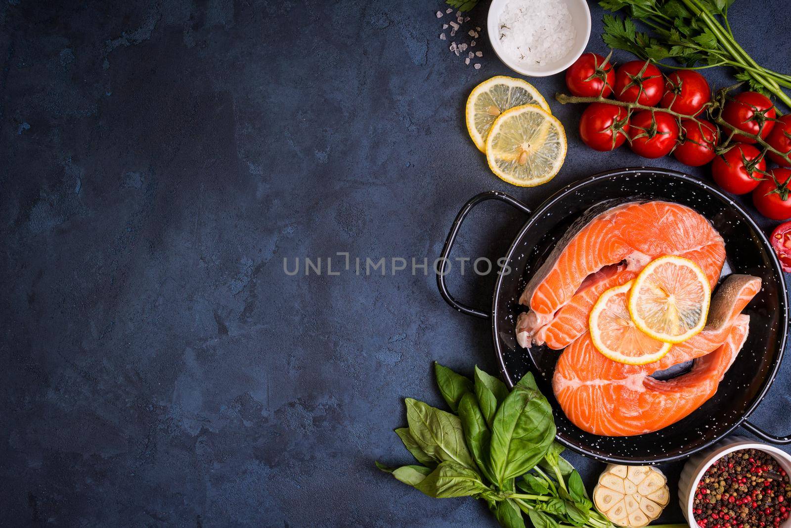 Raw fresh fish with vegetables ready to cook. Raw salmon steak with lemon and spices in a pan. Ingredients for cooking on a concrete background. Space for text. Diet and healthy food. Fish background