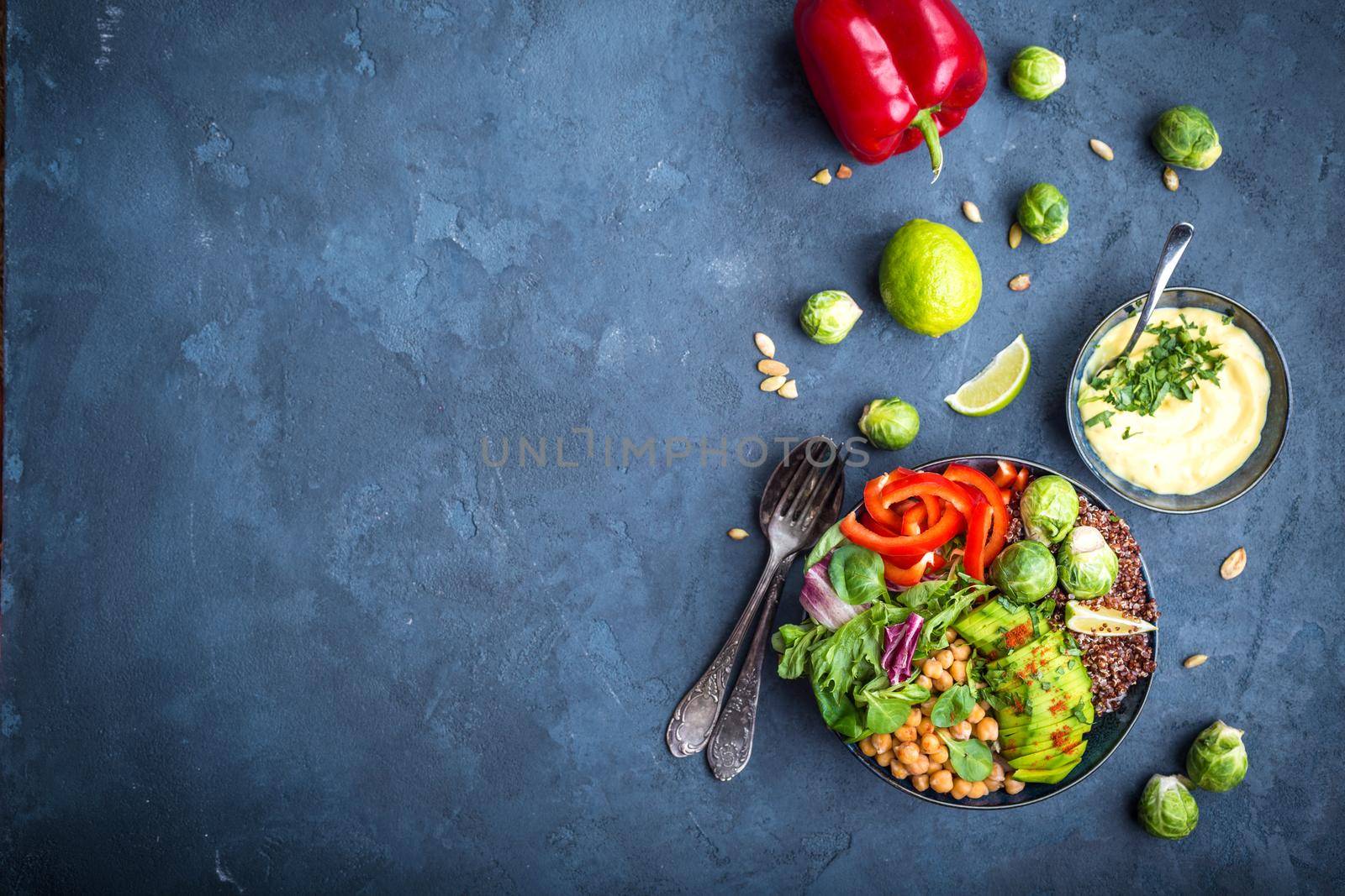 Bowl with healthy salad, dip, blue stone background. Top view. Space for text. Buddha bowl with chickpea, avocado, quinoa seeds, red bell pepper, fresh spinach, brussels sprout, lime. Vegetarian salad