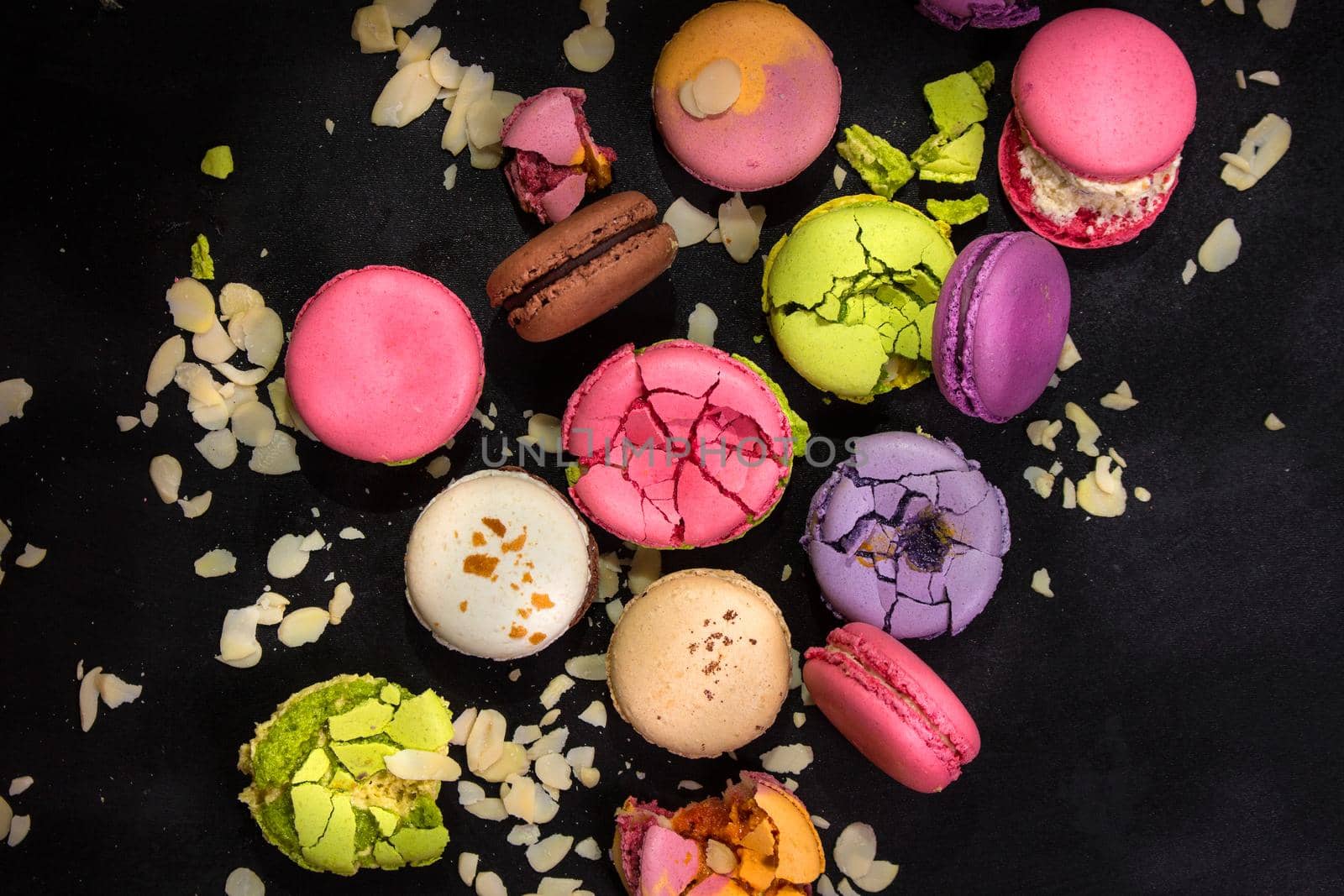 Assorted colorful french macarons and almond flakes on a black background. Closeup. Top view. Concept of the baking macarons