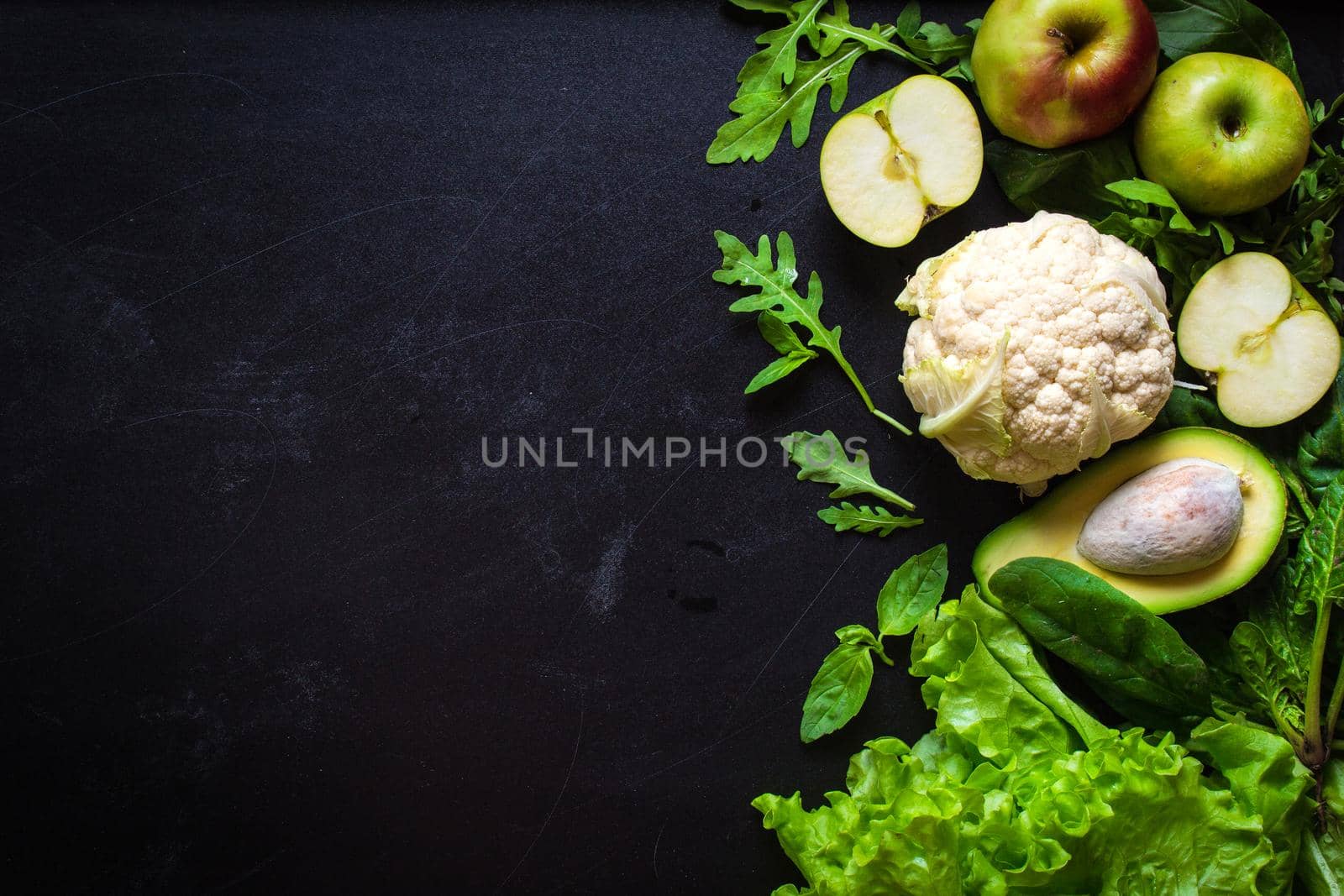 Fresh green vegetables and fruits on black chalk board background. Сauliflower, avocado, spinach, lettuce salad, green apples, herbs. Vegetarian food. Diet/healthy/detox food concept. Space for text