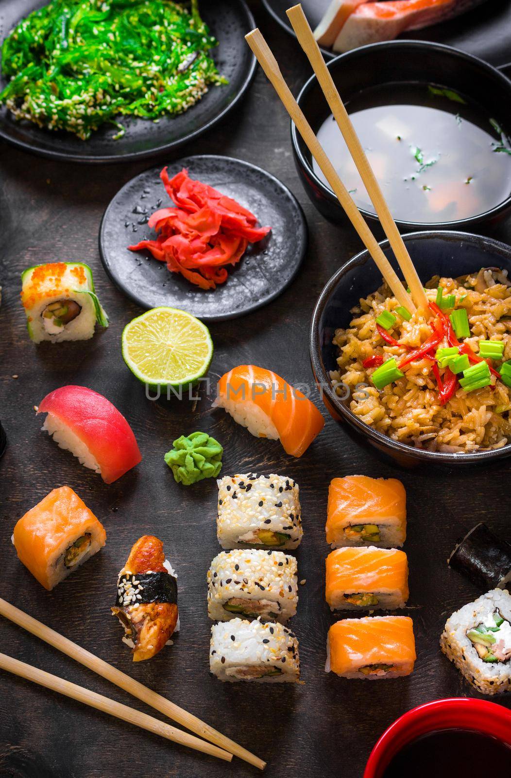 Table served with sushi and traditional japanese food on dark background. Sushi rolls, hiyashi wakame, miso soup, ramen, fried rice with vegetables, nigiri, soy sauce, сhopsticks. Japanese dishes set....