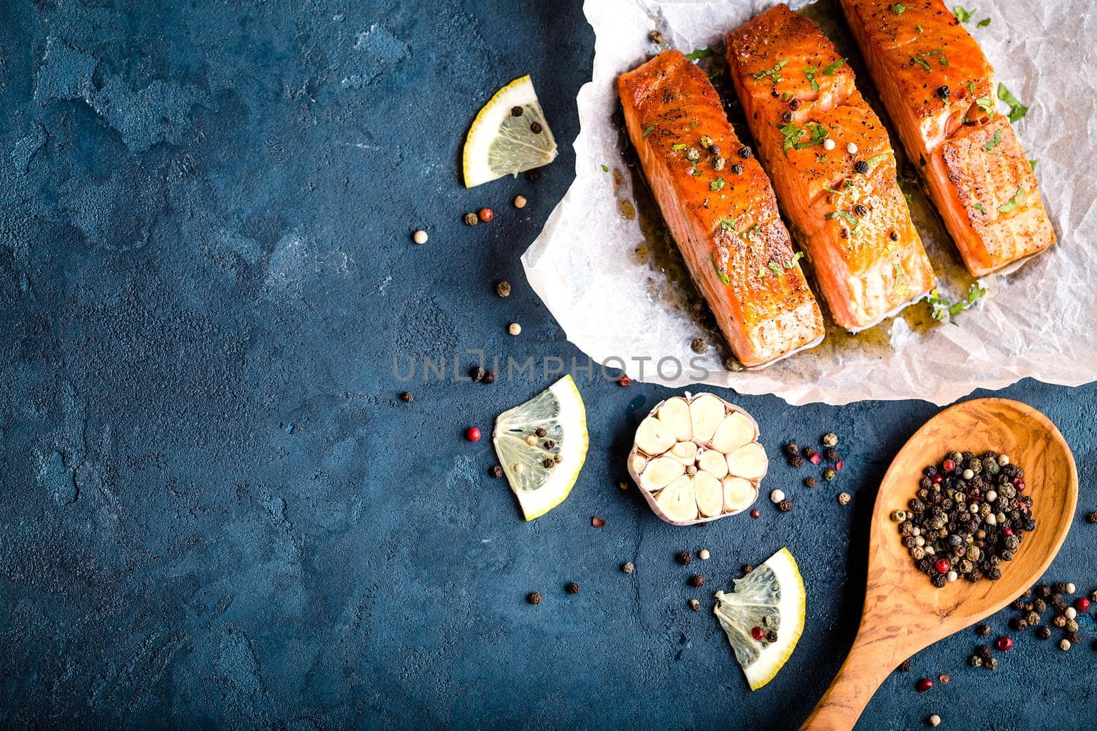 Delicious fried salmon fillet with seasonings on blue rustic concrete background. Cooked salmon steak with pepper, herbs, lemon, garlic, cooking spoon. Space for text. Fish for dinner. Healthy eating