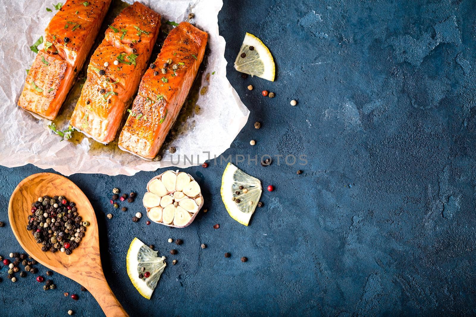 Delicious fried salmon fillet with seasonings on blue rustic concrete background. Cooked salmon steak with pepper, herbs, lemon, garlic, cooking spoon. Space for text. Fish for dinner. Healthy eating