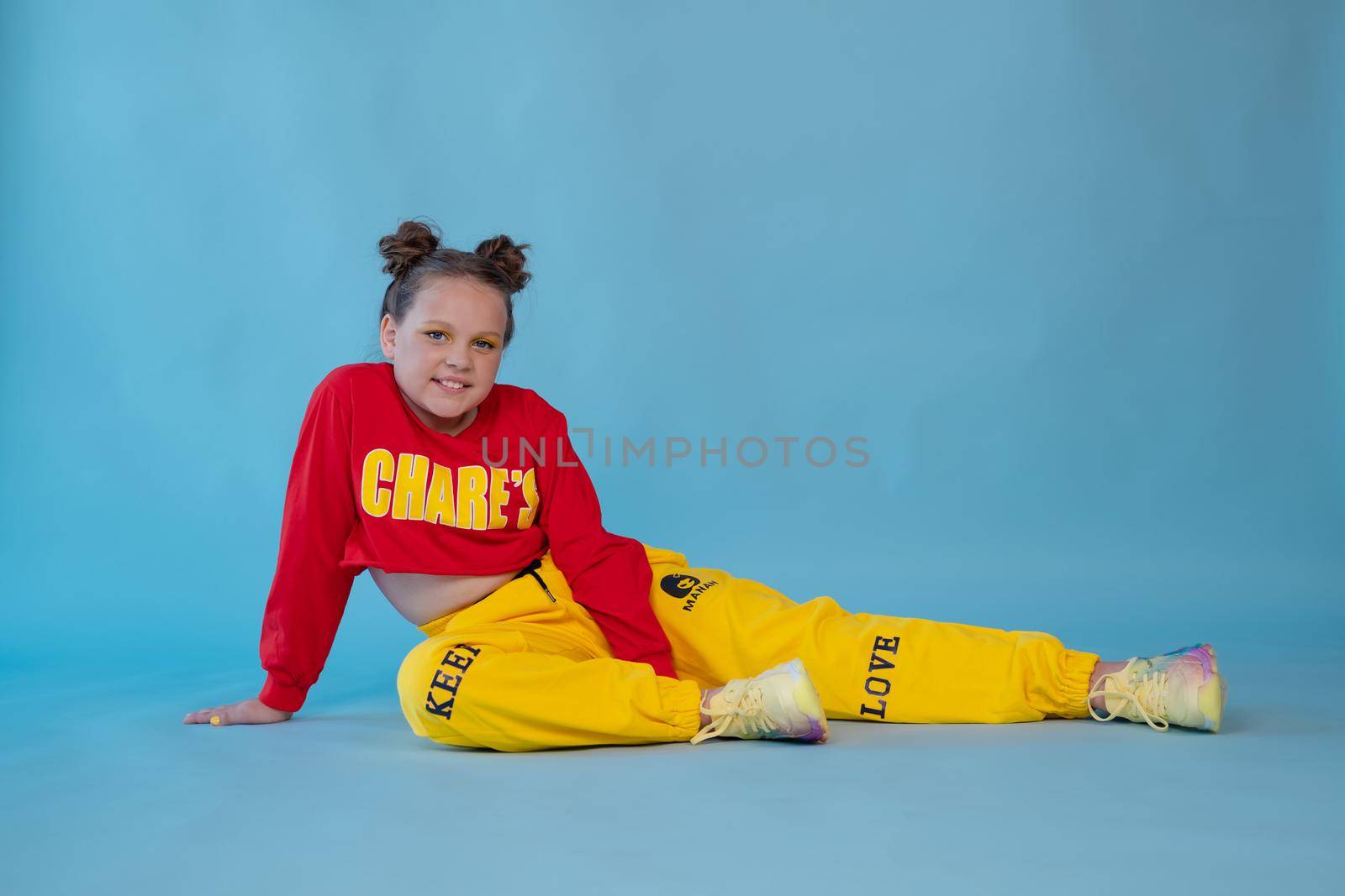 beauty portrait of stylish teenage girl in fashionable bright clothes. tween wearing red and yellow clothes on blue background. fashion portrait. two topknots. bright orange make up.