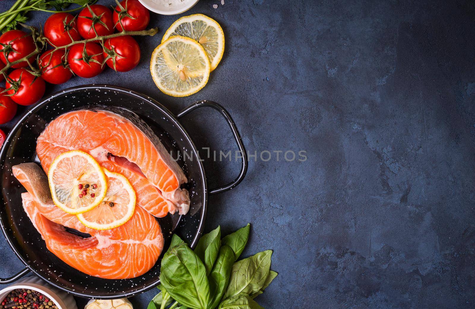 Raw fresh fish with vegetables ready to cook. Raw salmon steak with lemon and spices in a pan. Ingredients for cooking on a concrete background. Space for text. Diet and healthy food. Fish background