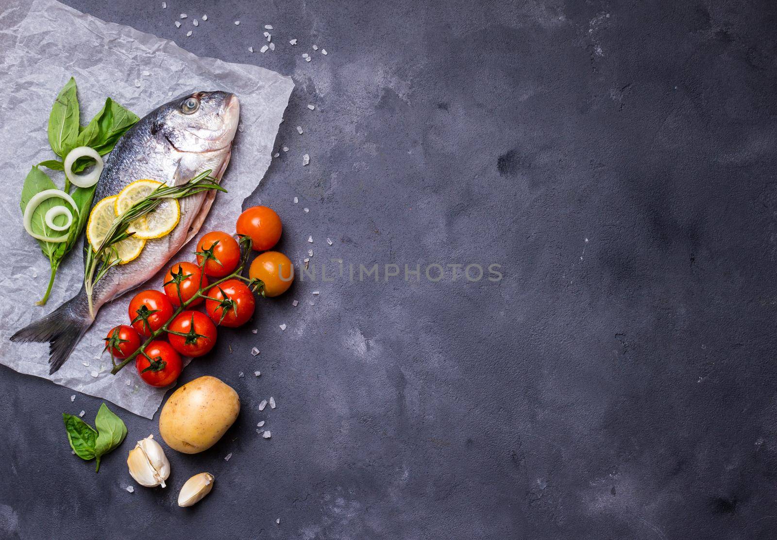 Raw fish with fresh ingredients ready to cook. Fish, lemon, herbs, potato, tomatoes. Ingredients for cooking on dark rustic background. Space for text. Diet and healthy food. Fish background. Top view