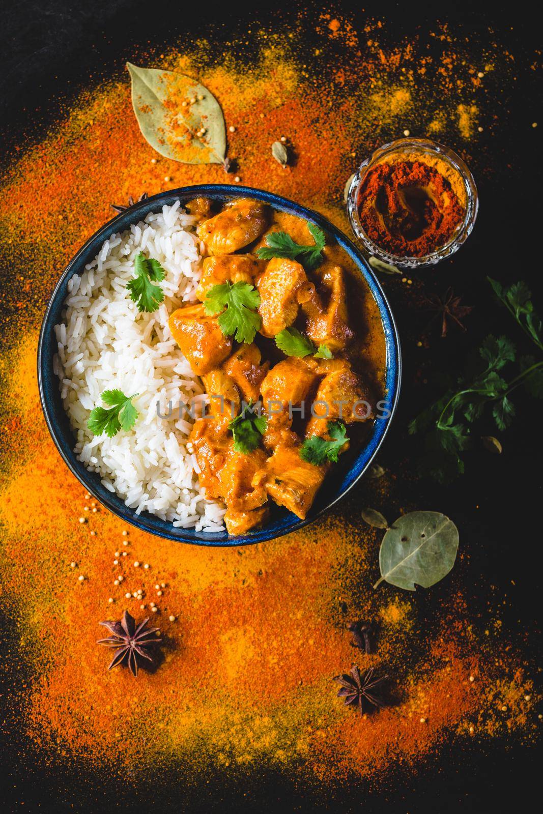 Indian Butter chicken with basmati rice, bowl, spices, black background. Indian style dinner. Butter chicken, traditional Indian dish. Top view. Chicken tikka masala. Indian cuisine concept. Overhead