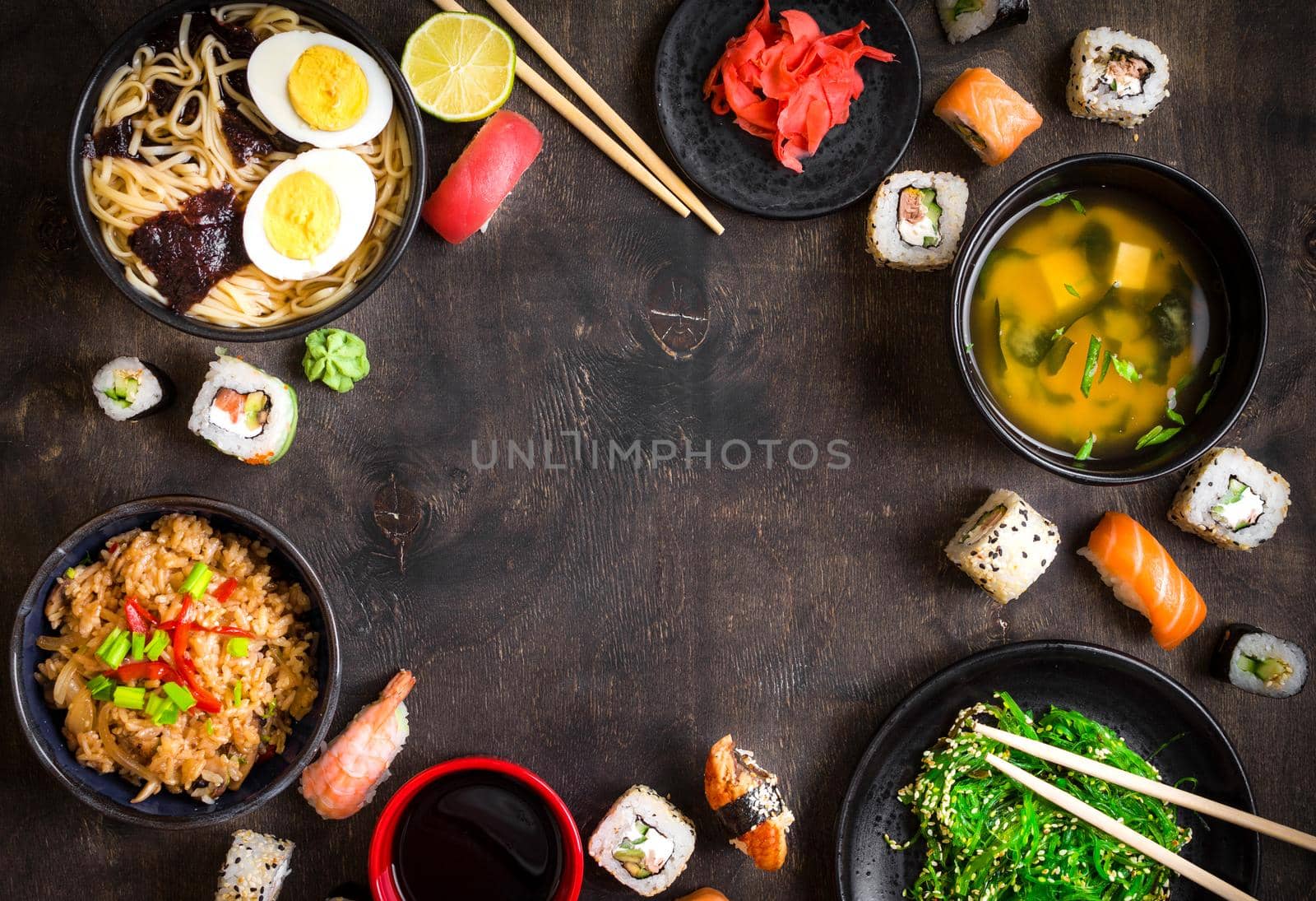 Sushi and japanese food on dark background. Sushi rolls, hiyashi wakame, miso soup, ramen, fried rice with vegetables, nigiri, salmon steak, soy sauce, сhopsticks. Asian/Japanese food frame. Overhead....