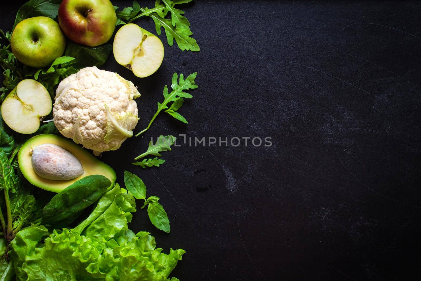 Fresh green vegetables and fruits on black chalk board background. Сauliflower, avocado, spinach, lettuce salad, green apples, herbs. Vegetarian food. Diet/healthy/detox food concept. Space for text