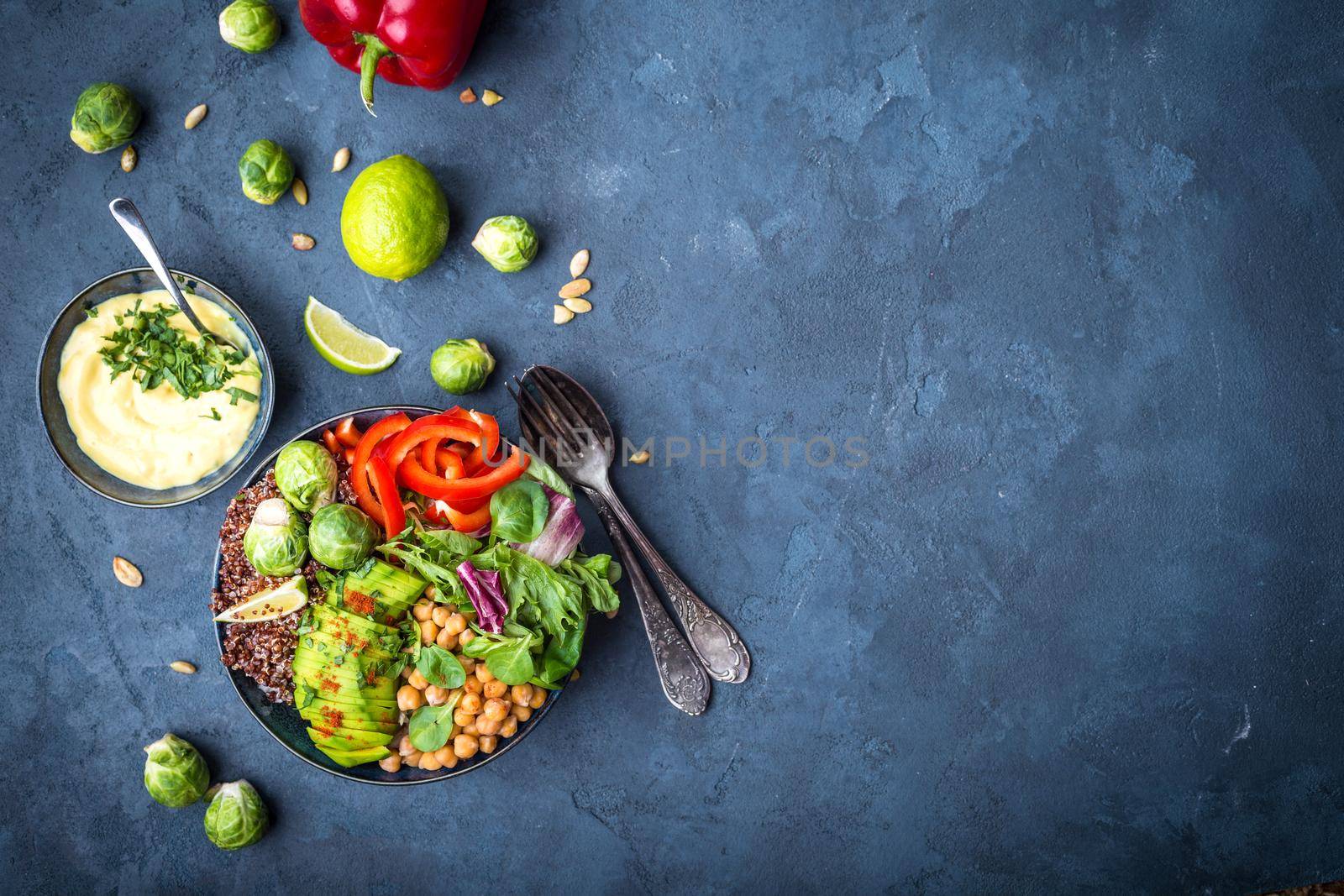 Bowl with healthy salad, dip, blue stone background. Top view. Space for text. Buddha bowl with chickpea, avocado, quinoa seeds, red bell pepper, fresh spinach, brussels sprout, lime. Vegetarian salad