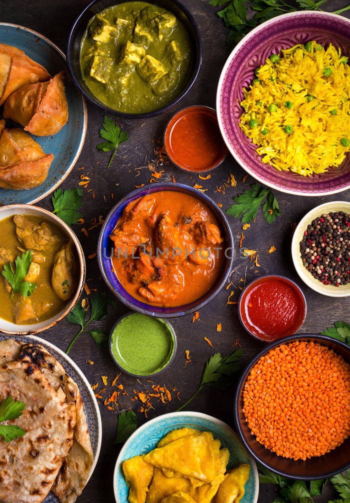 Assorted indian food on dark wooden background. Dishes and appetizers of indian cuisine. Curry, butter chicken, rice, lentils, paneer, samosa, naan, chutney, spices. Bowls and plates with indian food