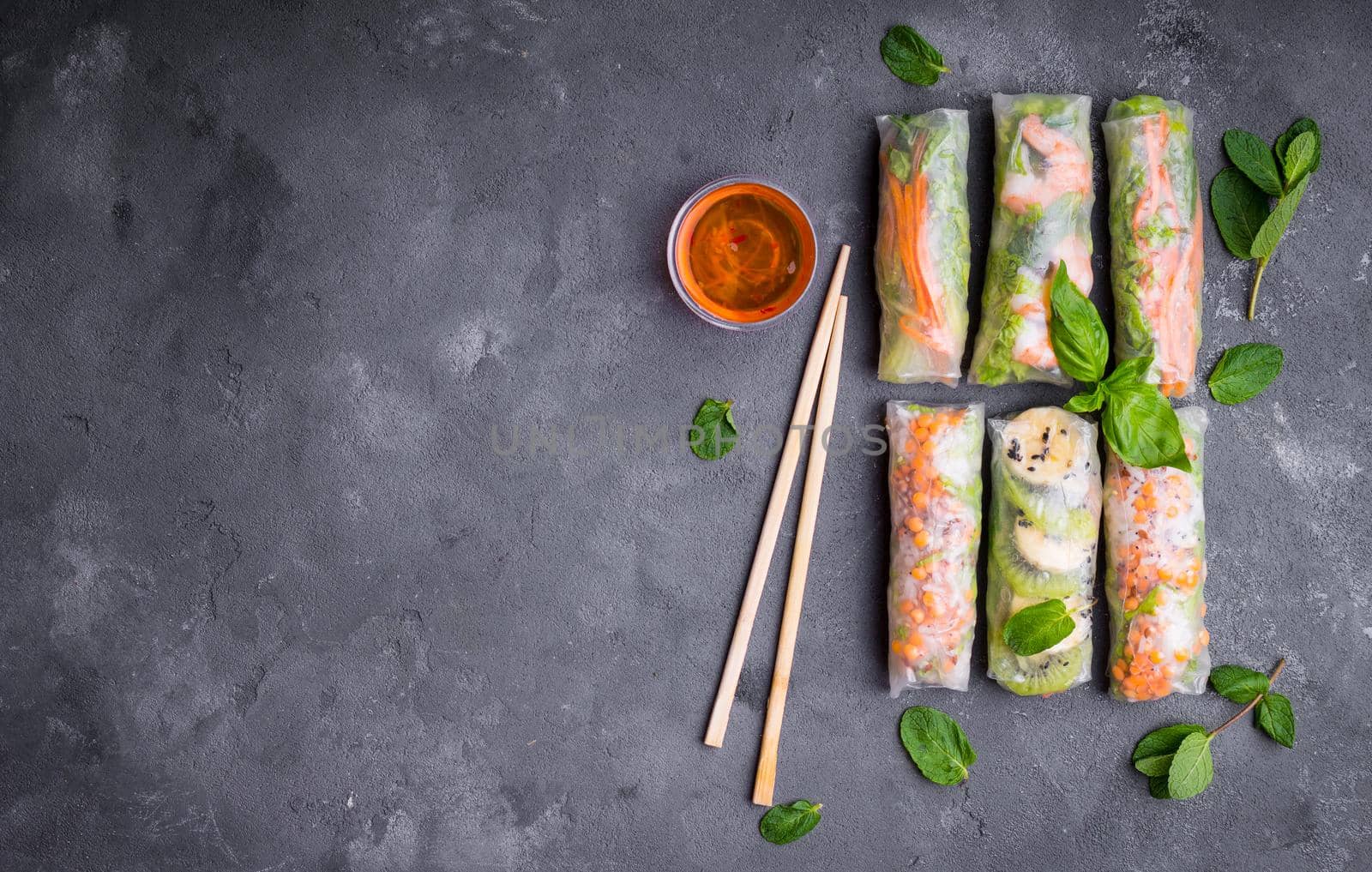 Fresh assorted spring rolls set background. Handmade asian/Chinese spring rolls, sauce, chopsticks. Rustic concrete background. Spring rolls with shrimps, vegetables, fruits. Space for text. Top view